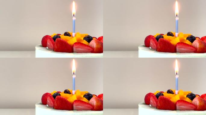 美味的生日蛋糕，水果蛋糕(新鲜的草莓，蓝莓和芒果)与淡蓝色蜡烛点燃火焰，在框架的右侧