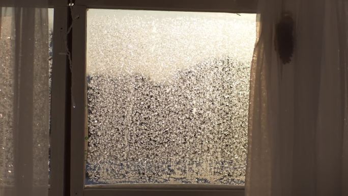 在阳光明媚的冬日里，玻璃上的美丽纹理与冰冻图案的特写。在明亮的阳光背景下，窗户玻璃上的霜冻自然图案特