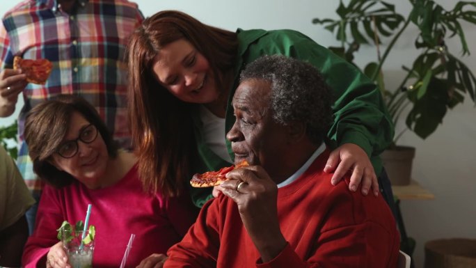 一位非裔美国老人正在和他的朋友和家人一起吃披萨