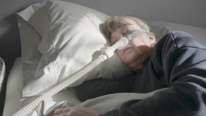 患有睡眠呼吸暂停的中年妇女躺在床上，戴着CPAP(持续气道正压通气)机辅助睡眠，戴着睡眠面罩