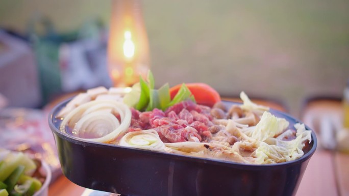 户外火锅用餐体验，新鲜蔬菜和切成薄片的牛肉，在露营灯的照亮下