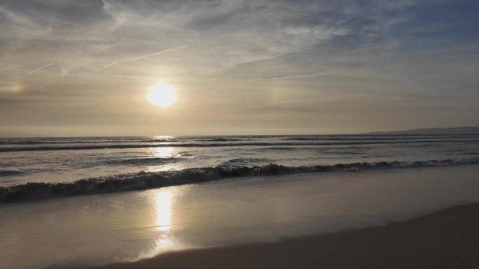 海浪翻滚到沙滩上，背景是蓝色的天空和戏剧性的雷云，日落，美丽的风景