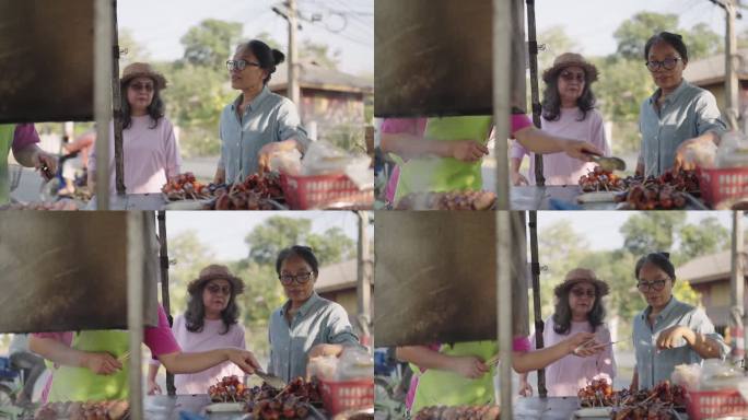 两名妇女在当地露天市场挑选烧烤食品，其中一人指着选择。