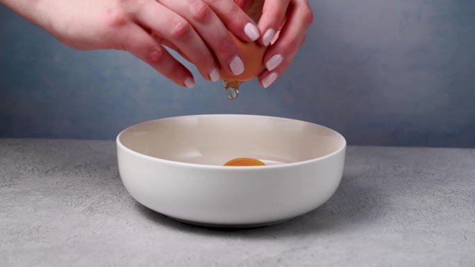 女人的手拿着一个有裂缝的鸡蛋，然后把它打碎。做煎蛋卷，早餐或烘焙。蛋白质食物
