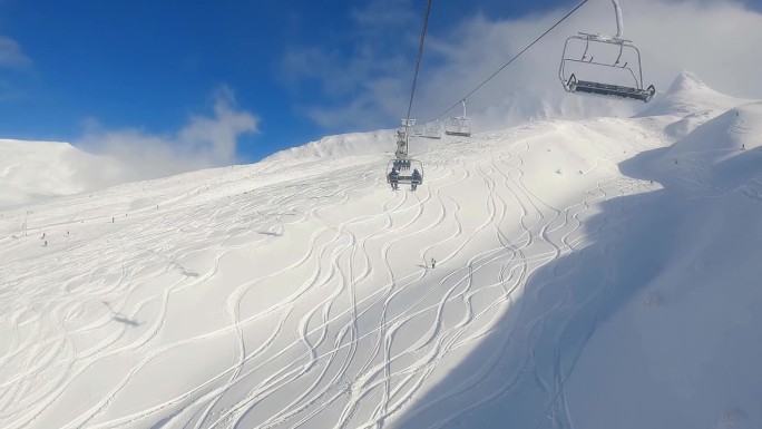 双人缆车第一人称视角，在阳光明媚的蓝天上，滑雪道在粉和滑雪者下面