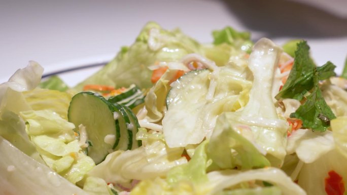 用一双筷子从盛满蔬菜的碗里挑一些蔬菜，上面淋上沙拉酱。