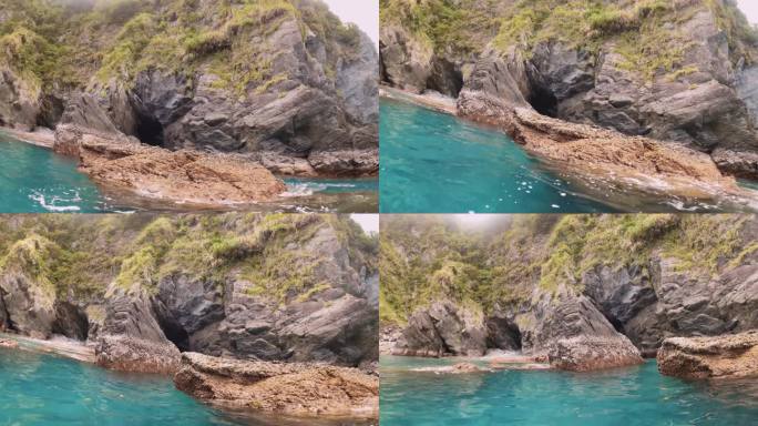 在蓝色的海洋表面游泳，海水咸水水平视图，眺望海岸海岸线上的侵蚀洞穴岩层，岩石和石头的巨石和植被白天多