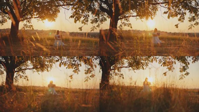 SLO莫多莉拍摄的母亲抱着婴儿，跪在球场上对天空在明亮的日落。一位母亲带着孩子在树下。