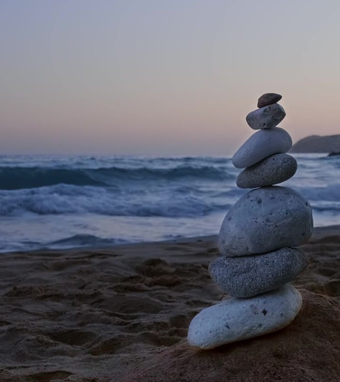 日落时在沙滩上平衡石头。背景是岩石和海浪。禅的概念，放松，冥想，脆弱