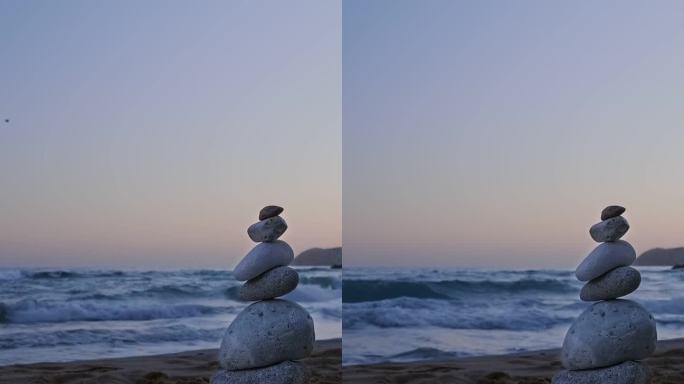 日落时在沙滩上平衡石头。背景是岩石和海浪。禅的概念，放松，冥想，脆弱
