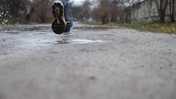 年轻运动员沿着乡间小路慢跑时踩进水坑的双腿。运动型男子在雨中沿着乡间小路奔跑的双脚。运动服户外训练的
