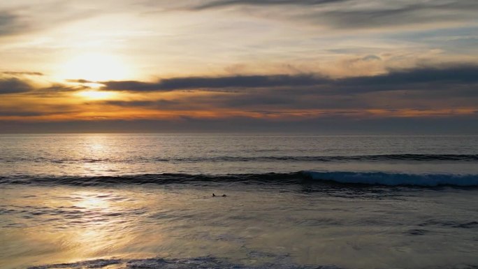 4K无人机拍摄的冲浪者在美丽的日落时捕捉海浪的画面。