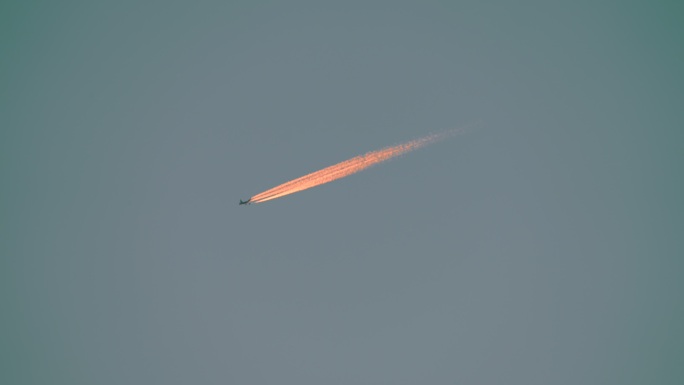 天空中的飞机和尾流折射阳光形成的橙色尾巴