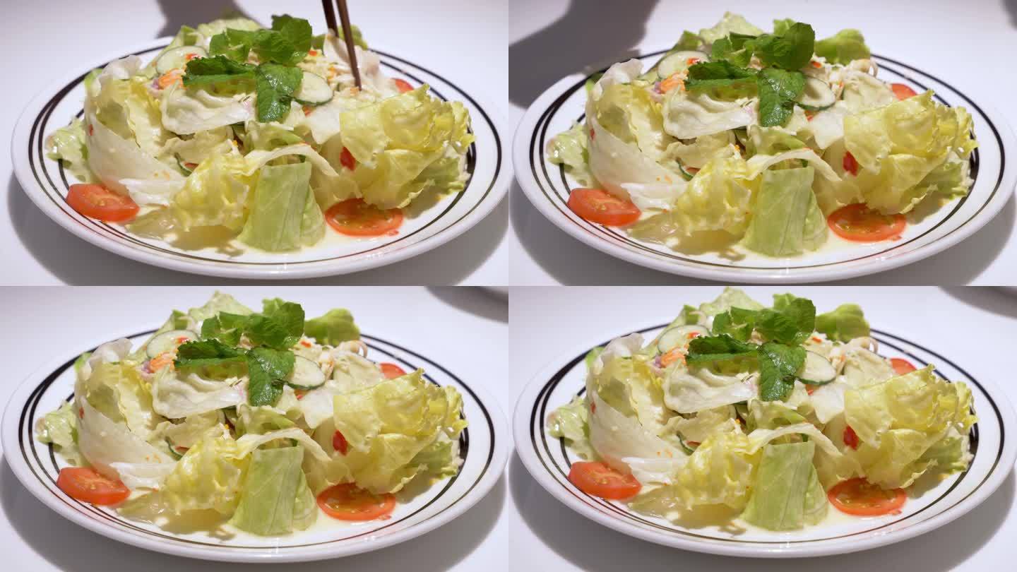 一盘蔬菜沙拉的特写，由黄瓜、生菜、西红柿、胡萝卜混合而成，上面撒上薄荷，淋上醋沙司。