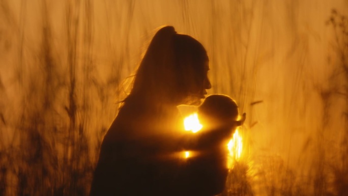 在橙色的天空中，母亲在明亮的阳光下亲吻婴儿男孩的额头