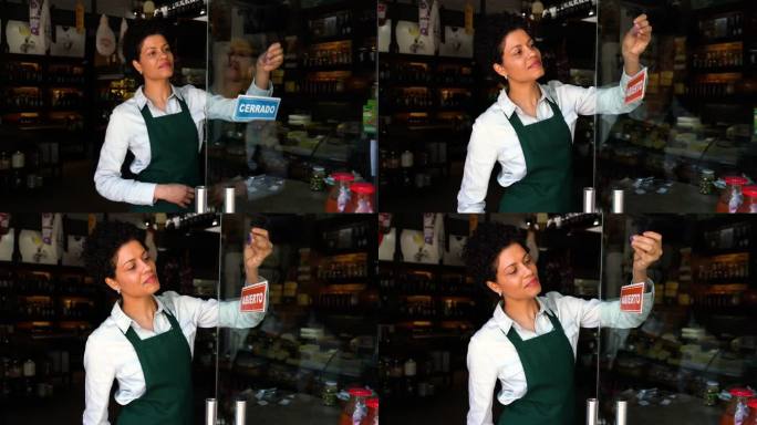 拉丁美洲一家开业的熟食店老板的视频肖像，他把开门的牌子挂在门上，然后面对镜头微笑