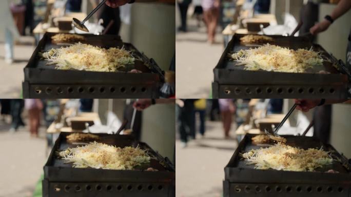 在日本的街头小吃中，一名男子在做日式烧饼前给面条加调味料。