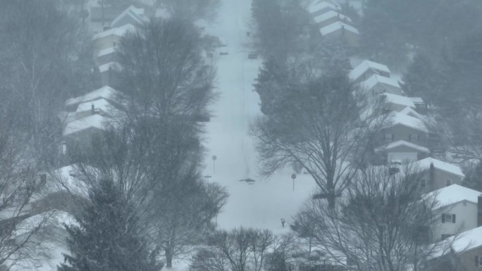 暴风雪中的住宅街道，房屋被雪覆盖，能见度变白。冬季在美国附近的空中拍摄。