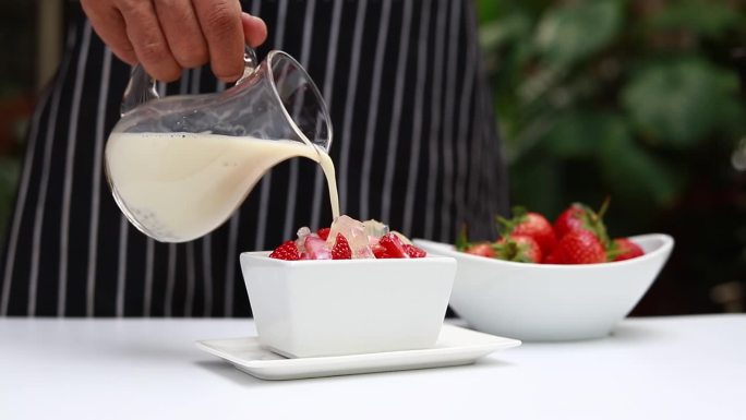 把牛奶倒进草莓碗里。美味的新鲜牛奶，白色盘子里有草莓和一杯牛奶