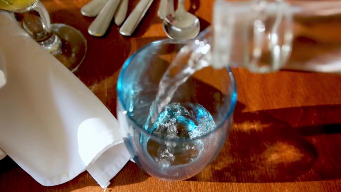 玻璃瓶装水被倒进桌子上的杯子里的慢动作镜头。