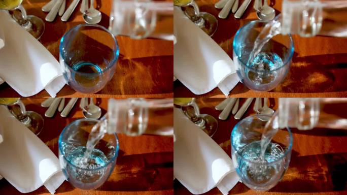 玻璃瓶装水被倒进桌子上的杯子里的慢动作镜头。