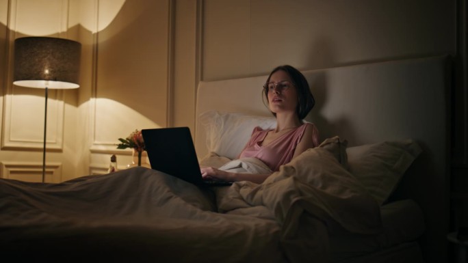晚归的自由职业者在床上休息。严肃的女人在电脑上打字