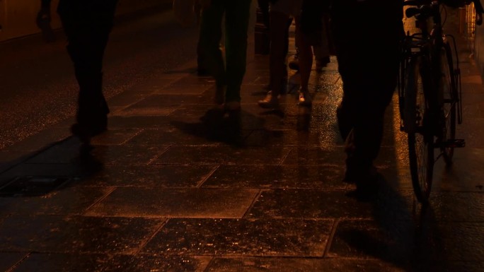 特写:在一个下雨的晚上，城市人的脚走在闪闪发光的湿人行道上