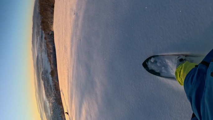 垂直视角:在一个美丽的阳光明媚的早晨，滑雪板运动员在雪地上滑行