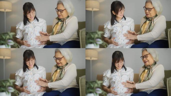 亚洲老年妇女抚摸怀孕女儿的肚子，在客厅与女儿交谈。