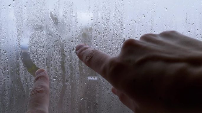 女人用手指在潮湿、雾蒙蒙的窗户上画两颗心。特写镜头