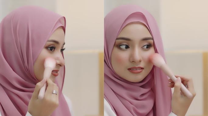 年轻的亚洲美丽的穆斯林妇女戴着头巾照镜子，每天在家里用脸颊刷化妆。漂亮的女孩在脸上刷妆。
