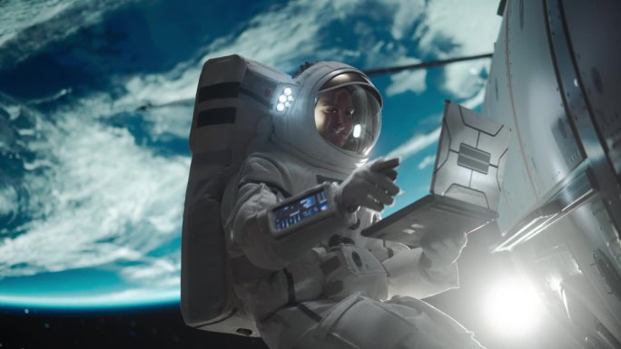 一个穿着太空服的人在维修卫星的同时，在外太空随意地摆弄着笔记本电脑。宇航员写信给任务控制中心，家人或