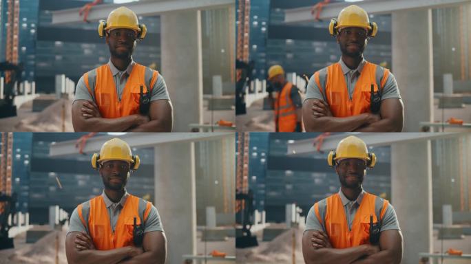 穿着安全制服和安全帽在住宅楼施工现场工作的快乐专业重工业工程师。微笑的非裔美国人工业现场经理站在户外
