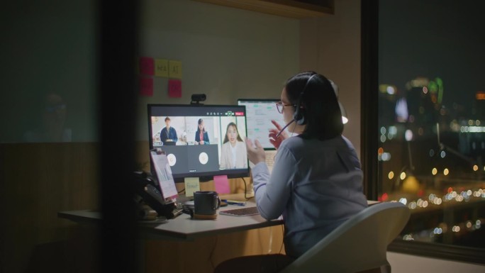 亚洲女商人视频通话，在昏暗的光线下独自在办公室工作到很晚