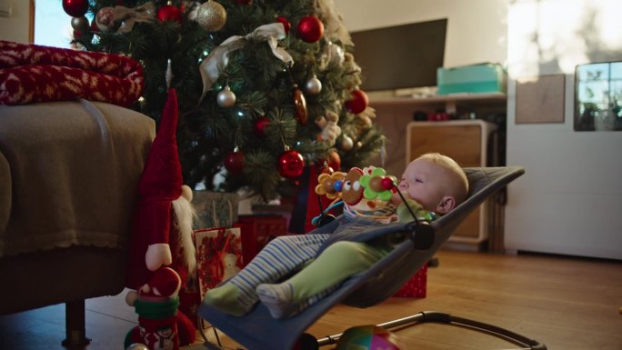 在家里客厅装饰的圣诞树旁，小男孩在Bouncer上玩耍的慢镜头