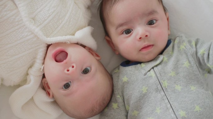 可爱的刚出生的双胞胎宝宝男孩和女孩一起躺在家里的床上。