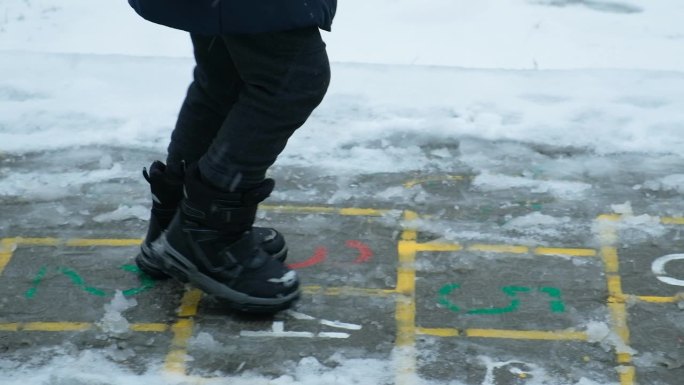 小孩子穿着靴子在外面下雪时蹦蹦跳跳。冬天的衣服，童鞋
