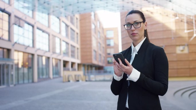 白人女商人在大城市街道上使用智能手机的肖像。自信的管理者在工作休息时间上网、发信息、上网