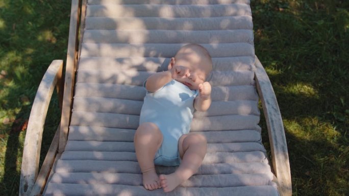 在阳光明媚的日子里，可爱的小男孩斜倚在草坪的躺椅上