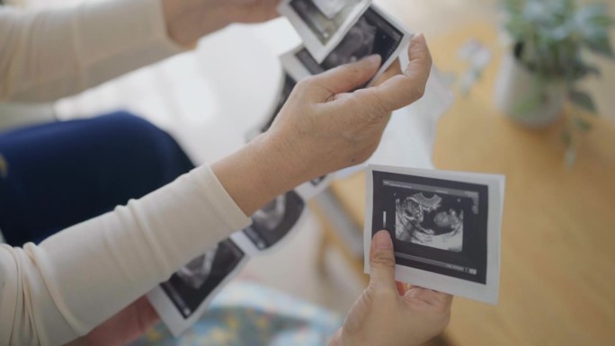 近距离的年轻孕妇和她的母亲考虑照片超声婴儿在家里的客厅
