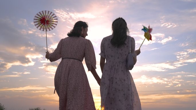 夕阳草坪美女手拉手爬山背影