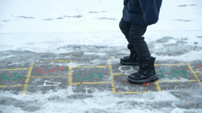 小孩子穿着靴子在外面下雪时蹦蹦跳跳。冬天的衣服，童鞋