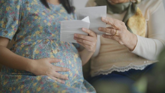 孕妇和她的母亲在家里抚摸腹部时看超声波图像