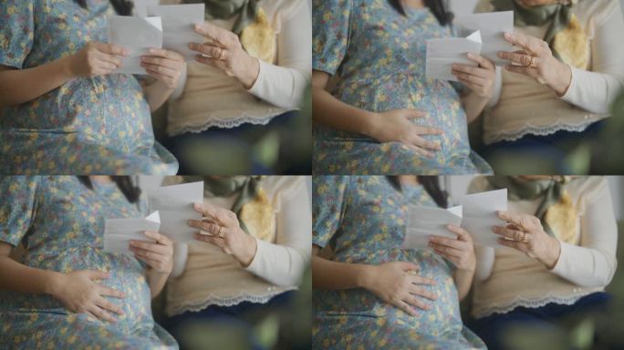 孕妇和她的母亲在家里抚摸腹部时看超声波图像