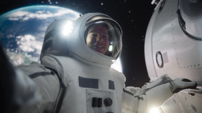 屏幕替换概念，一个年轻的宇航员漂浮在零重力的太空中，以地球为背景进行视频通话。工程师在开放空间使用智