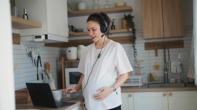 聪明的孕妇在现代化的厨房里利用电脑与同事见面
