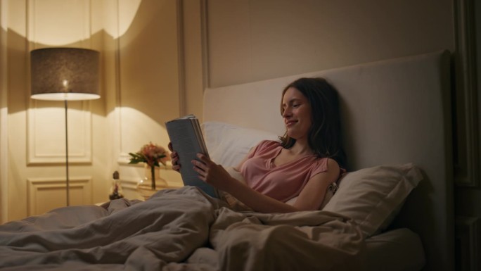 安静的女人晚上在家看书。微笑的读者享受小说的休息