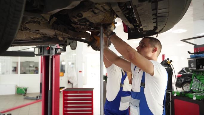 汽车技师在现代化车间统一安装变速箱，修理汽车离合器。专业人员使用工具进行车辆传动系统的维修，并在提高