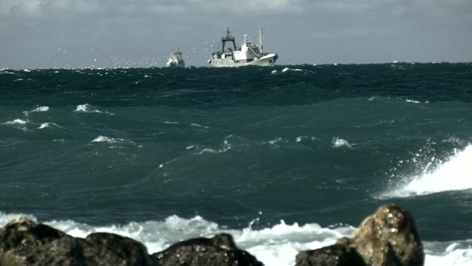 暴风雨的海浪冲击着海岸，一艘渔船在海上(慢动作)