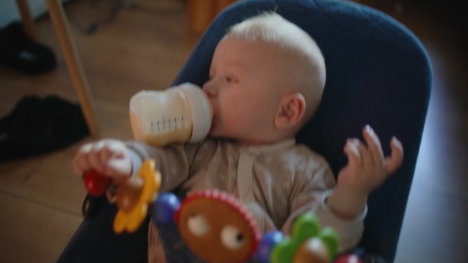 SLO高角度手持拍摄可爱的小男孩在家里被妈妈喂奶瓶里的牛奶